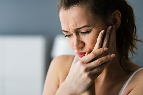 Woman holding her left cheek. She looks in pain